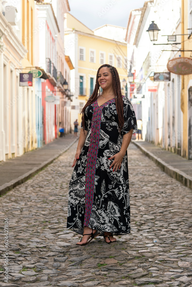 Portrait of a pretty woman standing on the old cobblestone street of Pelourinho, a tourist on a trip, with braids in her hair. Old houses in the background.