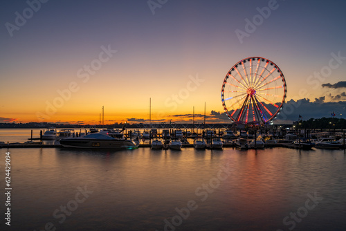 Illuminated ferris wheel at National Harbor near the nation capital of Washington DC at sunset with marina in the foreground © steheap
