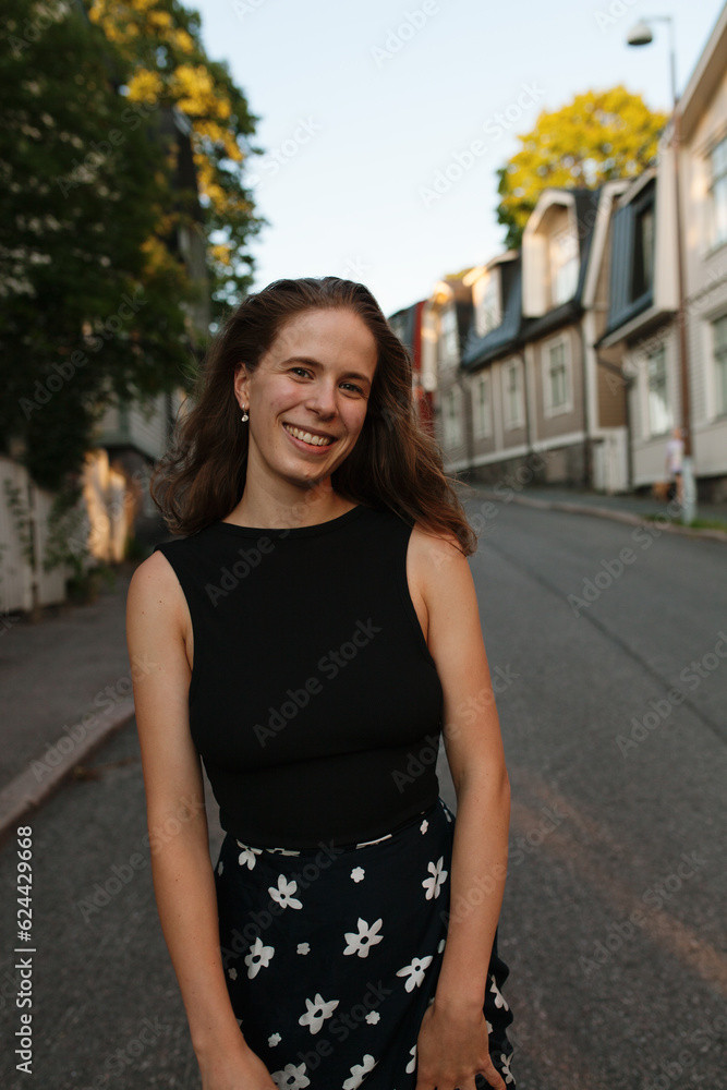 Fototapeta premium Smiling young woman standing on a calm neighbourhood road in Helsinki, Finland