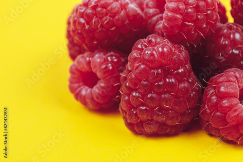 Heap of fresh ripe and sweet raspberries on yellow background. Red raspberries. Macro shot.