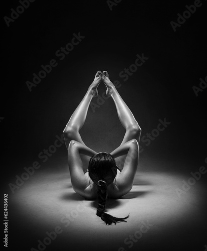 Beautiful nude sexy fitness girl with great figure flexing her perfect body in a yoga pose at the studio. Black and white photo