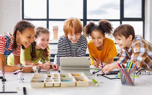 Cheerful  schoolkids   looking at tablet screen and celebrate   successful completion of collective school work   during online lesson photo