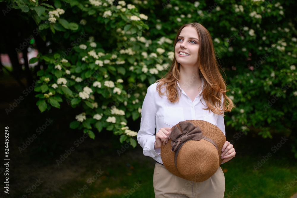 Portrait on a summer day near a jasmine bush of a happy female tourist with a straw hat in her hands, while on vacation Portrait on a summer day near a jasmine bush of a happy female tourist with a straw hat in her hands, while on vacation