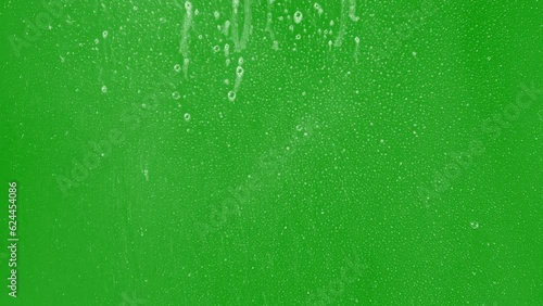 Foam dripping on glass with a greenscreen background with small bubbles and mist