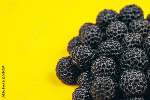 Heap of fresh ripe and sweet raspberries on yellow background. Black raspberries. Macro shot.