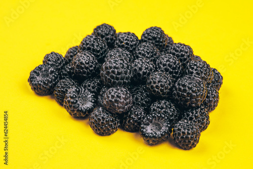 Heap of fresh ripe and sweet raspberries on yellow background. Black raspberries. Macro shot.