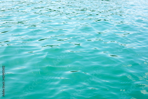 Abstract nature textured background, water waves in the lake with sun reflection, clear blue-green water