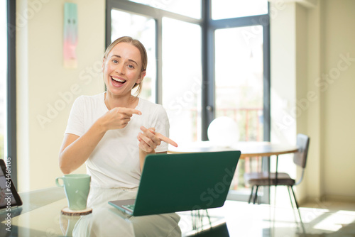 caucasian pretty woman with a laptop smiling cheerfully and pointing to copy space on palm on the side, showing or advertising an object