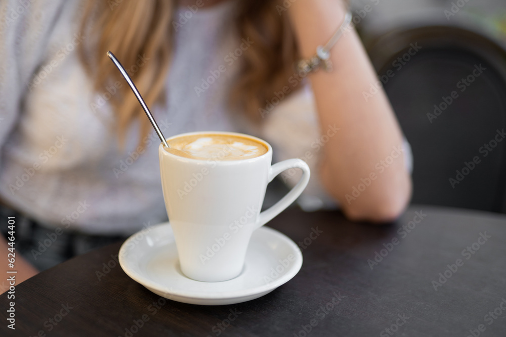 close-up of a girl's hand holding a cup of coffee at a table in a cafe