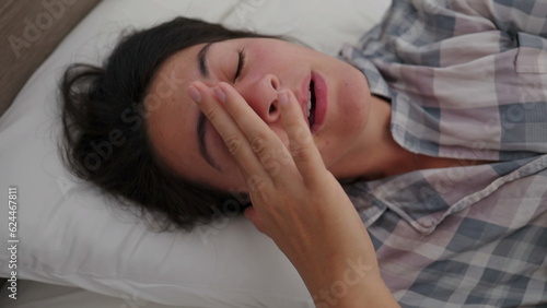 Woman yawning waking up in the morning lying in bed yawns rubbing eye and face