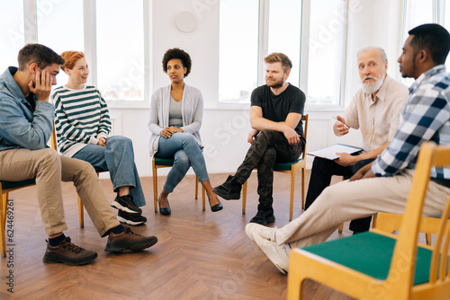 Fotografie, Obraz Wide shot of mature male psychotherapist leading therapy meeting with addicted diverse and different ages people sitting in circle during therapy meeting