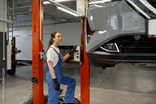 Young woman auto technician turning on car lift mechanism