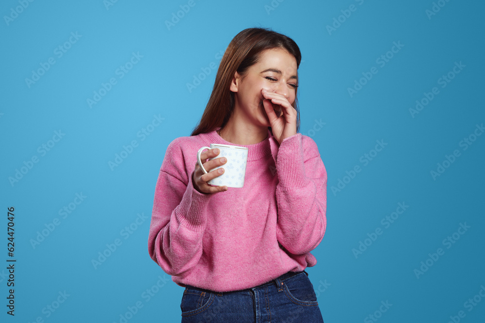 Portrait of brunette Hispanic girl with shy expression smiles pleasantly with cup of coffee wears pink jumper, isolated over blue background. People, emotions concept Portrait of brunette Hispanic girl with shy expression smiles pleasantly with cup of coffee wears pink jumper, isolated over blue background. People, emotions concept