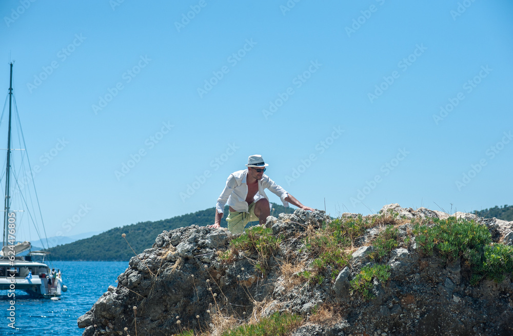 A tourist is trying to climb on the rock by the sea in Greece