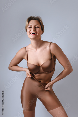 Portrait of young attractive woman wearing brown lingerie with high waist shaping briefs against gray background