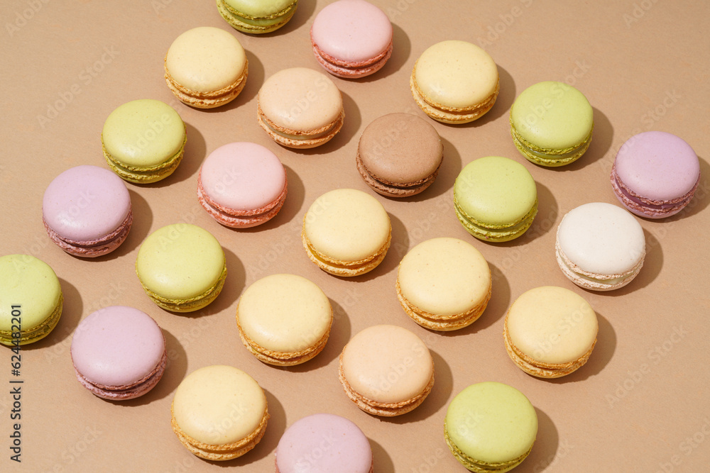 Fototapeta premium An overhead shot of a beige table surface featuring an array of colorful macarons in neat rows
