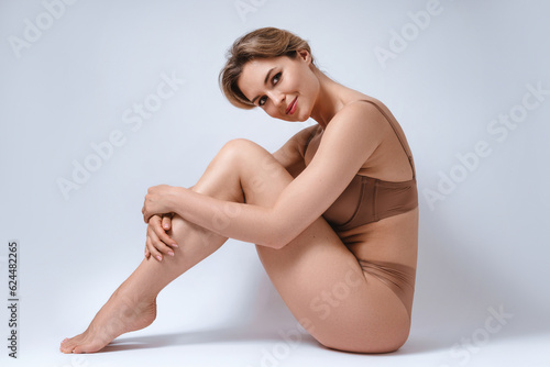 Young attractive woman wearing brown lingerie is happy with her body and smooth skin