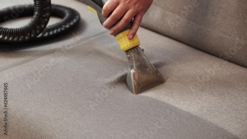 Dry cleaner's man employee removing dirt from furniture in flat, closeup, vacuum clean sofa with professional equipment. cleaning sofa with washing suction cleaner closeup.