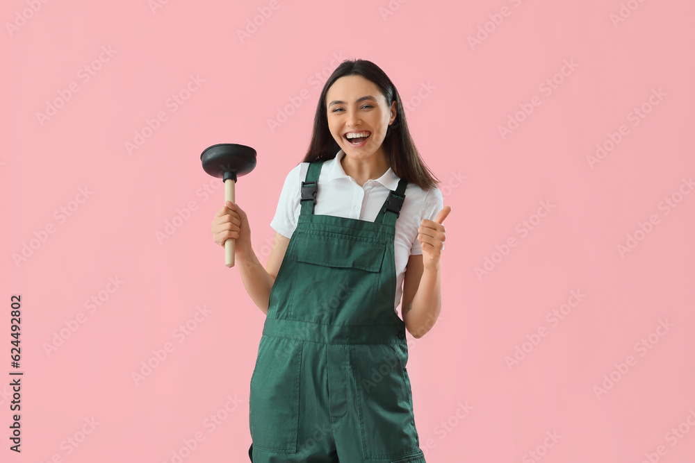 Happy female plumber with plunger showing thumb-up on pink background Happy female plumber with plunger showing thumb-up on pink background