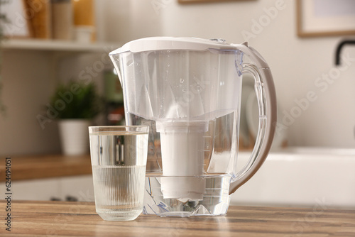 Glass of pure water and filter jug on wooden table in kitchen photo