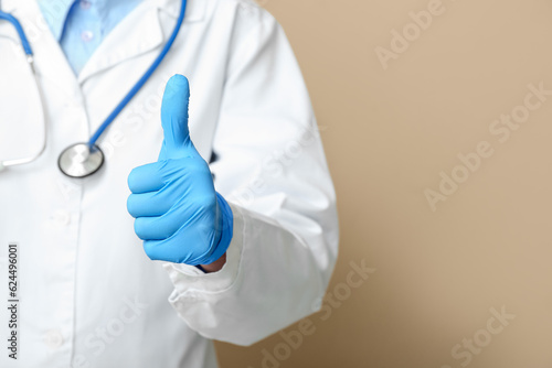 Female doctor with stethoscope showing thumb-up on beige background