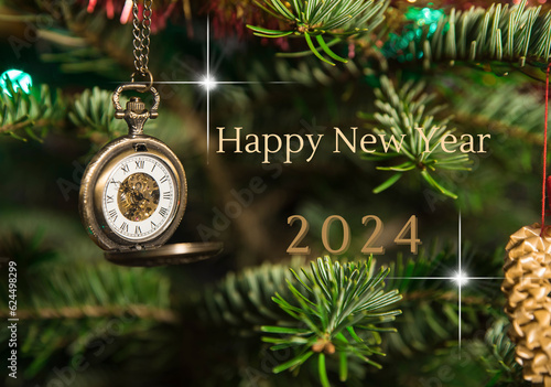 Życzenia Happy New Year 2024 na tle zielonej choinki z wiszącym otwieranym zegarkiem w stylu retro. photo