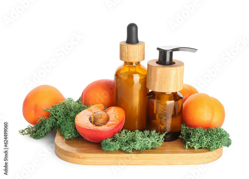 Wooden board with bottles of cosmetic products, ripe apricots and moss on white background
