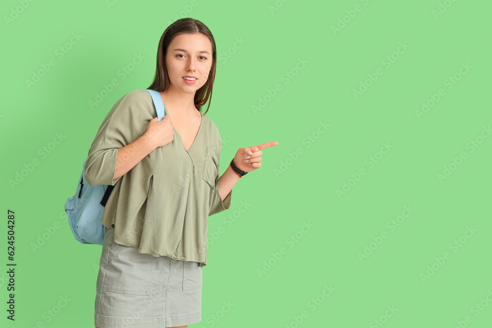 Female student pointing at something on green background Female student pointing at something on green background