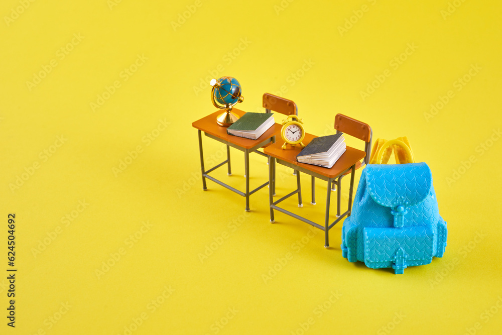 Fototapeta premium School desk with school accessory and blue backpack on yellow background