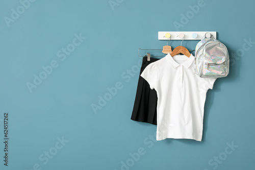 Stylish school uniform and backpack hanging on color wall