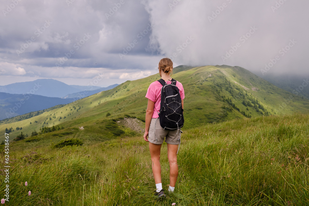 Naklejka premium Girl is watching on mountains view. Woman is hiking in mountains in summer.Beautiful mountain landscape in Carpathians, Romania.Travel and tourism.Woman hiker is enjoying the mountain view.