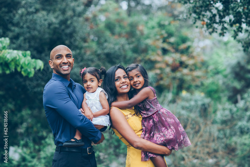 Fotografie beautiful indian family standing and smiling holding their kids in the park with