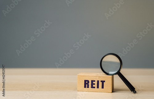 Reit inscription on a wooden block. Real estate investment trust concept. Company that owns, operates, or finances income-generating real estate. Magnifying glass