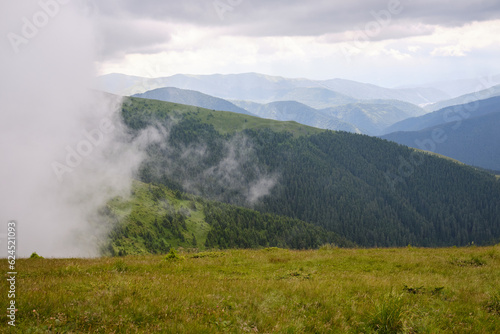 View on mountain valley in low clouds.Mountains in clouds. Carpathians mountains in Romania. Baiului Mountains trails.