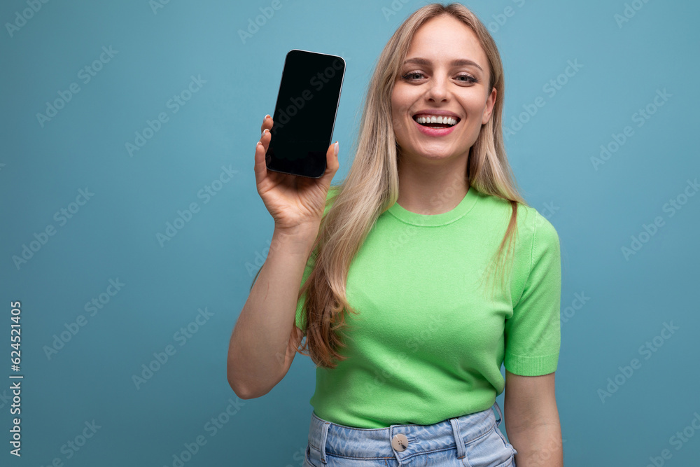 smiling bright blond girl in casual outfit holding smartphone with screen forward mockup on blue background