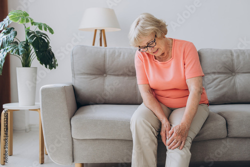 Senior woman suffering from pain in knee at home photo