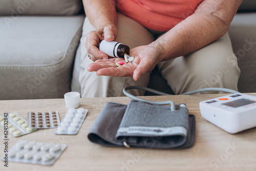 Sick older woman take care for health, using sphygmomanometer for measure blood pressure, pulse and heart rate by self and takes medication at home. photo