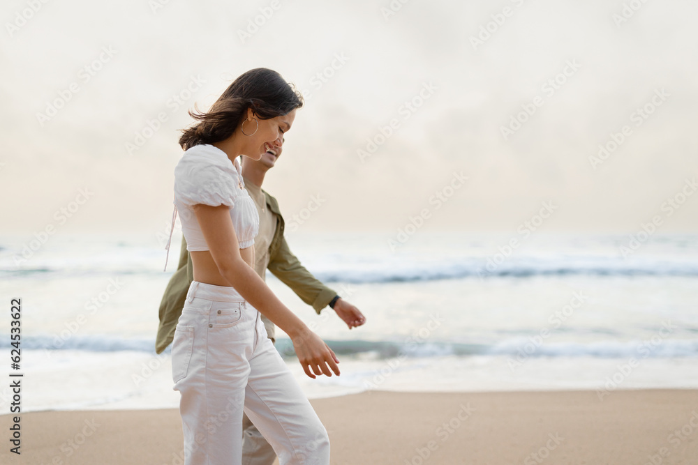 Young european couple of newlyweds walking, holding hands and enjoying time by the ocean, side view, free space Young european couple of newlyweds walking, holding hands and enjoying time by the ocean, side view, free space