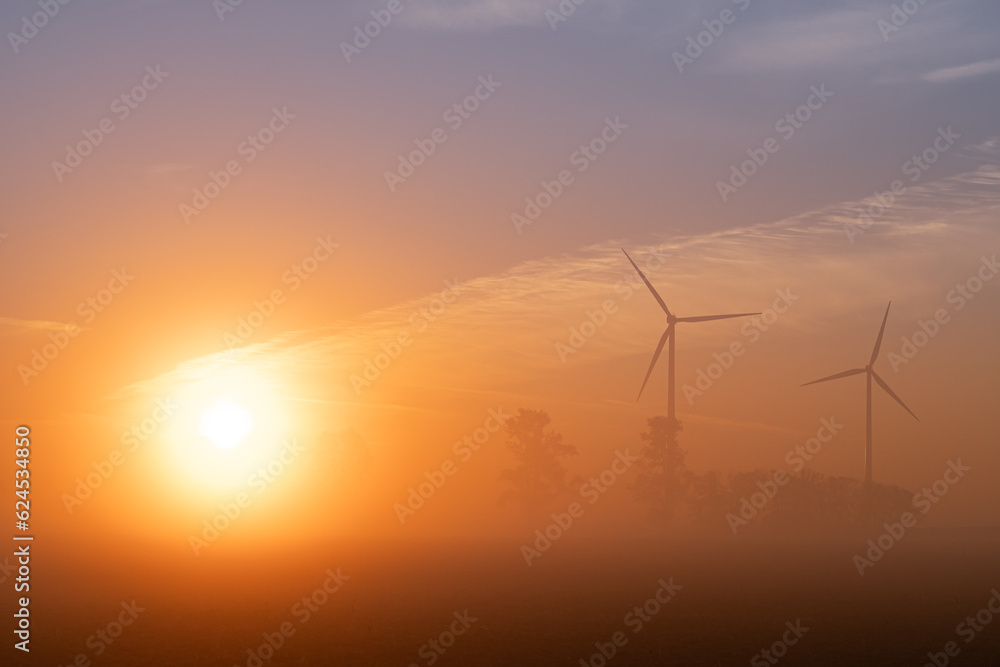 Sonnenaufgang im Nebel mit Windkraftanlagen im Hintergrund