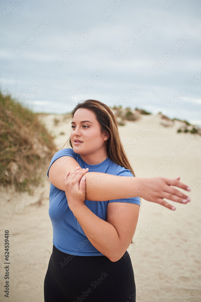 Body positive woman in sportive tracksuit stretching arms at the gloomy ocean beach Body positive woman in sportive tracksuit stretching arms at the gloomy ocean beach