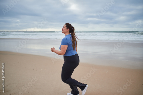 Young body positive sports woman running along the sandy sea shore