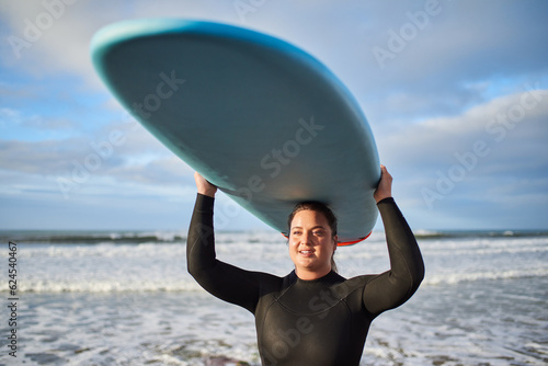 Happy full figured woman carrying surfboard at her head while preparing for the surf