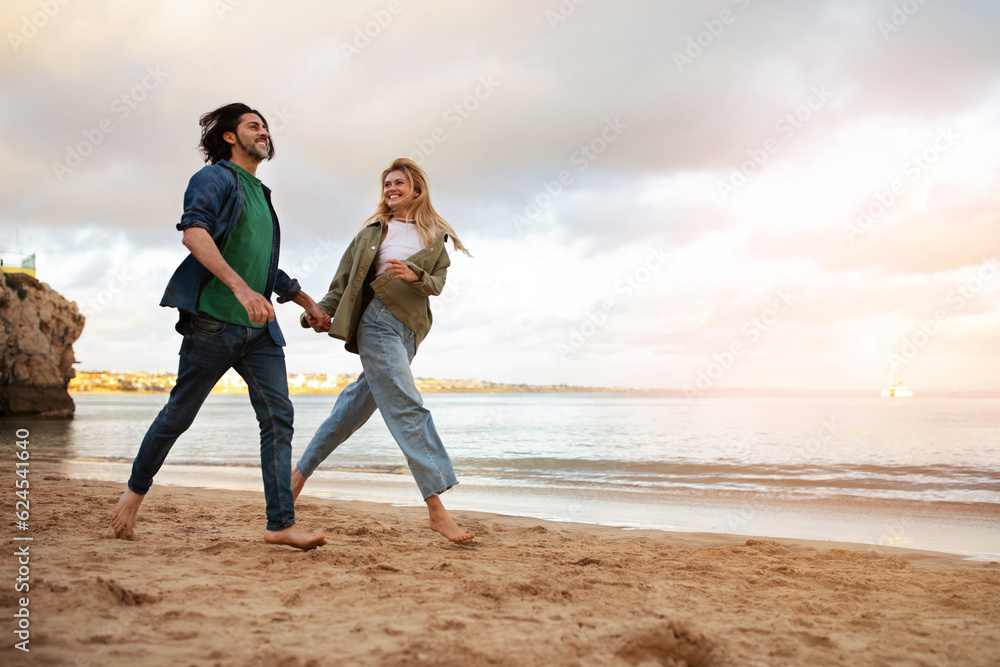 Happy young couple running on beach near sea, holding hands and smiling Happy young couple running on beach near sea, holding hands and smiling