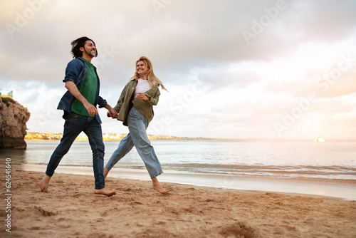 Happy young couple running on beach near sea, holding hands and smiling