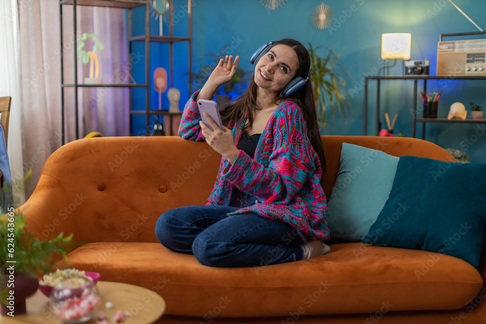 Obraz premium Happy overjoyed Caucasian woman in wireless headphones relaxing sitting on couch at home apartment choosing listening favorite energetic disco dancing music. People weekend daytime leisure activities