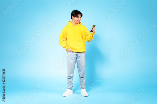 Chinese teenager guy using smartphone surfing internet standing in studio