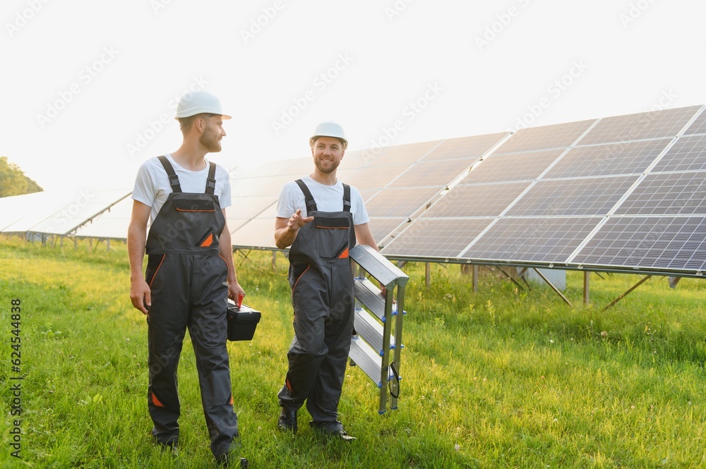 Two male electrician workers walking in between long rows of photovoltaic solar panels and talking about installation of new solar panels. Two male electrician workers walking in between long rows of photovoltaic solar panels and talking about installation of new solar panels.
