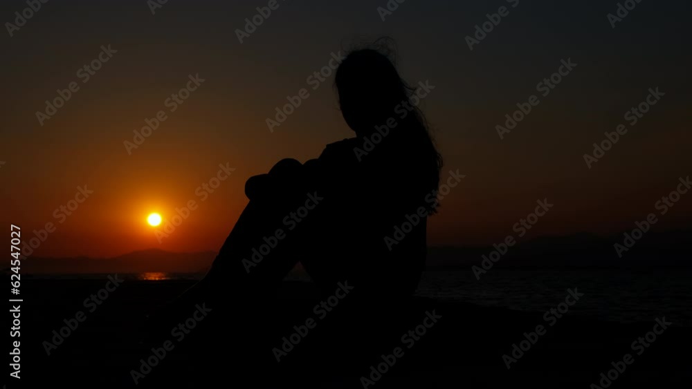 Teen silhouette against red sun. A sad teen girl silhouette sitting on the evening beach in loneliness during weekend. Teen silhouette against red sun. A sad teen girl silhouette sitting on the evening beach in loneliness during weekend.