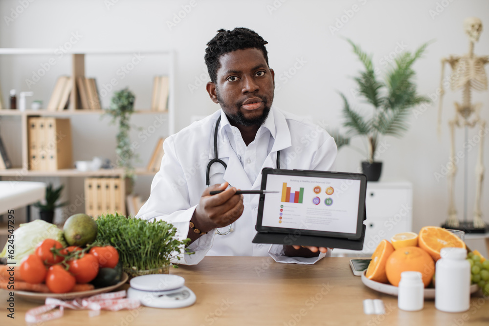 Male expert in dieting posing on camera with digital tablet and demonstrating scale of obesity among people with improper nutrition. Afican american professional offering courses for weight loss. Male expert in dieting posing on camera with digital tablet and demonstrating scale of obesity among people with improper nutrition. Afican american professional offering courses for weight loss.