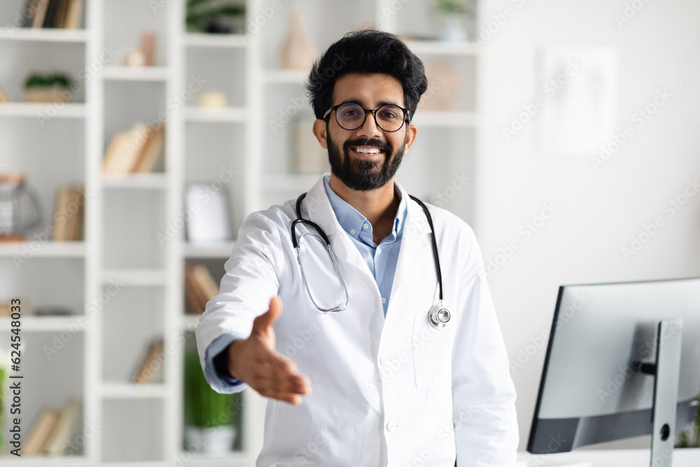 Friendly handsome middle eastern doctor outstretching hand and smiling Friendly handsome middle eastern doctor outstretching hand and smiling